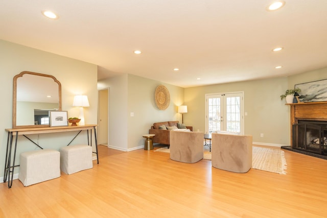 living room with recessed lighting, a fireplace with raised hearth, french doors, and wood finished floors