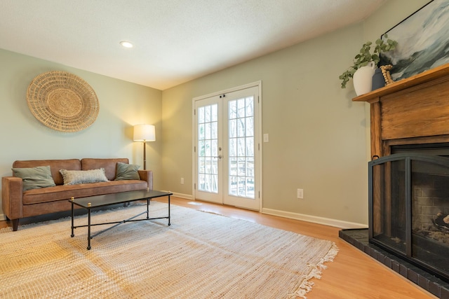 living area with french doors, wood finished floors, baseboards, and a fireplace with raised hearth