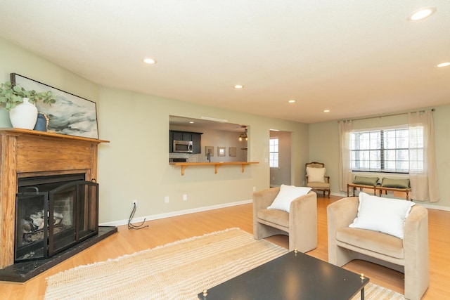 living area with recessed lighting, a fireplace with raised hearth, baseboards, and wood finished floors