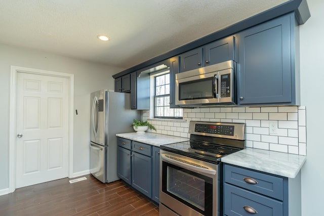 kitchen featuring baseboards, blue cabinetry, stainless steel appliances, dark wood-type flooring, and tasteful backsplash