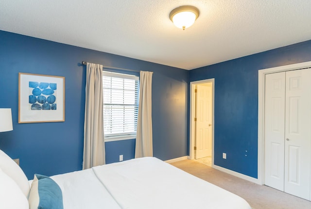 bedroom featuring a closet, light colored carpet, a textured ceiling, and baseboards