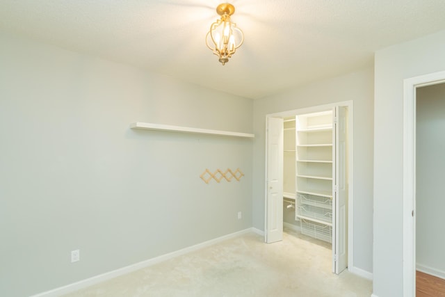 unfurnished bedroom featuring a walk in closet, a textured ceiling, a closet, carpet, and baseboards