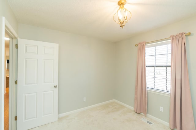 unfurnished room with a textured ceiling, baseboards, visible vents, and light carpet