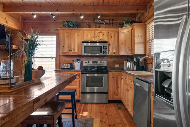 kitchen with dark countertops, wooden walls, appliances with stainless steel finishes, light wood-style floors, and a sink