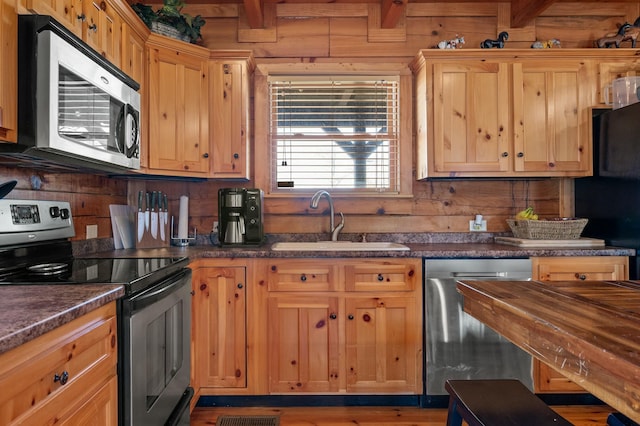 kitchen featuring a sink, wooden walls, and appliances with stainless steel finishes