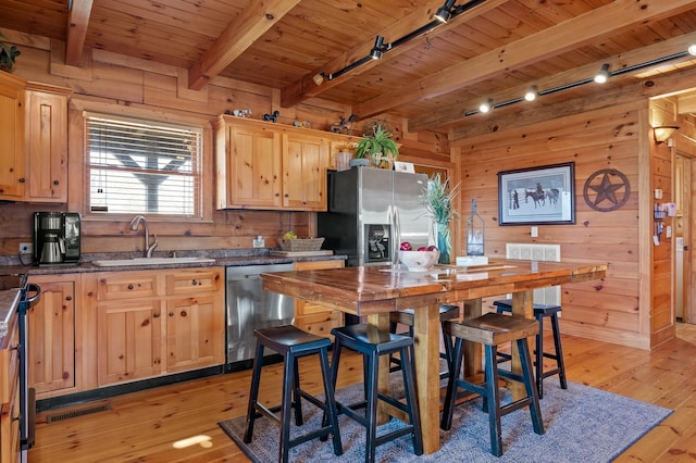 kitchen with wooden walls, light brown cabinets, a sink, appliances with stainless steel finishes, and light wood-type flooring