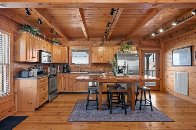 kitchen with wooden walls, visible vents, light brown cabinetry, and stainless steel appliances