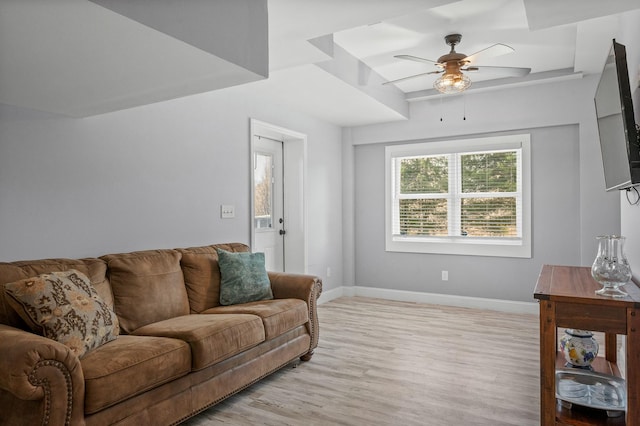 living room with a raised ceiling, a ceiling fan, baseboards, and light wood-type flooring