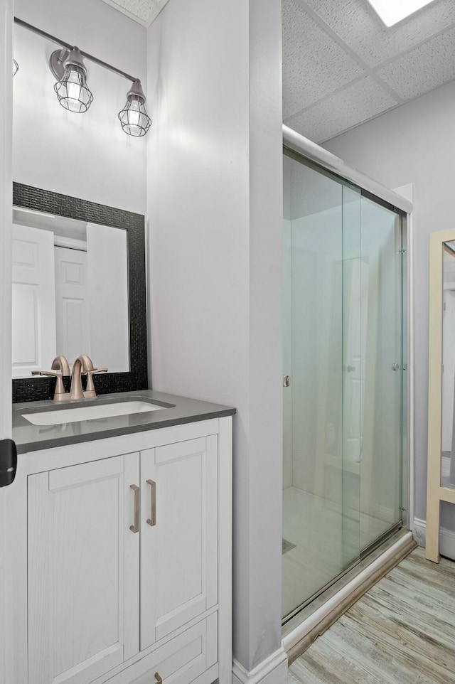 full bathroom featuring a paneled ceiling, wood finished floors, a stall shower, and vanity