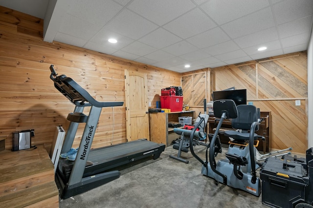 workout room featuring recessed lighting, a drop ceiling, and wood walls