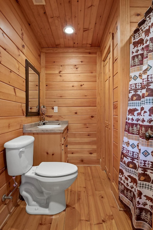 bathroom with wooden walls, wood ceiling, toilet, wood finished floors, and vanity