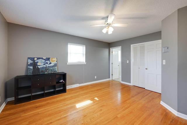 interior space featuring wood finished floors, baseboards, ceiling fan, a closet, and a textured ceiling