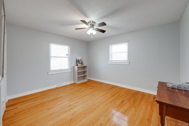 spare room with visible vents, ceiling fan, baseboards, light wood-style floors, and a textured ceiling
