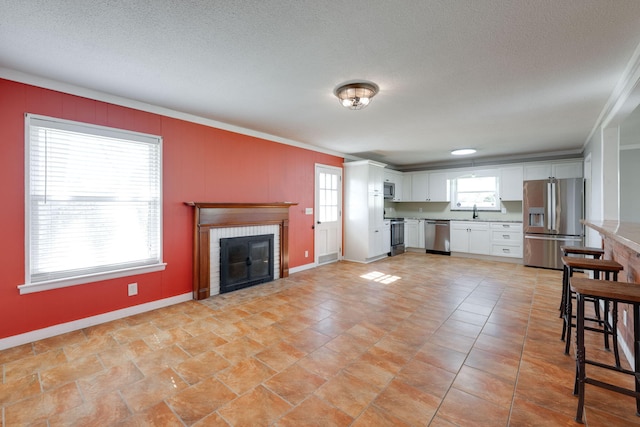 kitchen featuring a textured ceiling, stainless steel appliances, white cabinets, a fireplace, and light countertops