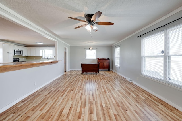 unfurnished living room featuring light wood-type flooring, ornamental molding, a ceiling fan, a textured ceiling, and baseboards