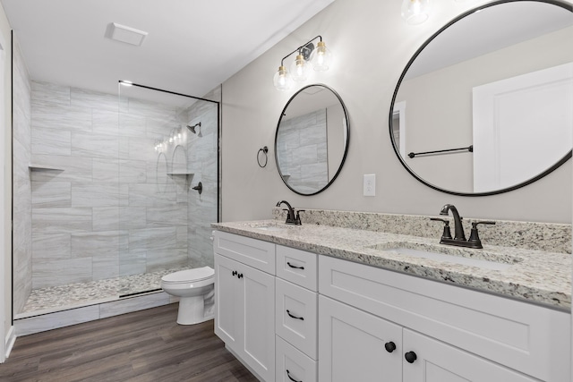 bathroom featuring wood finished floors, tiled shower, toilet, and a sink