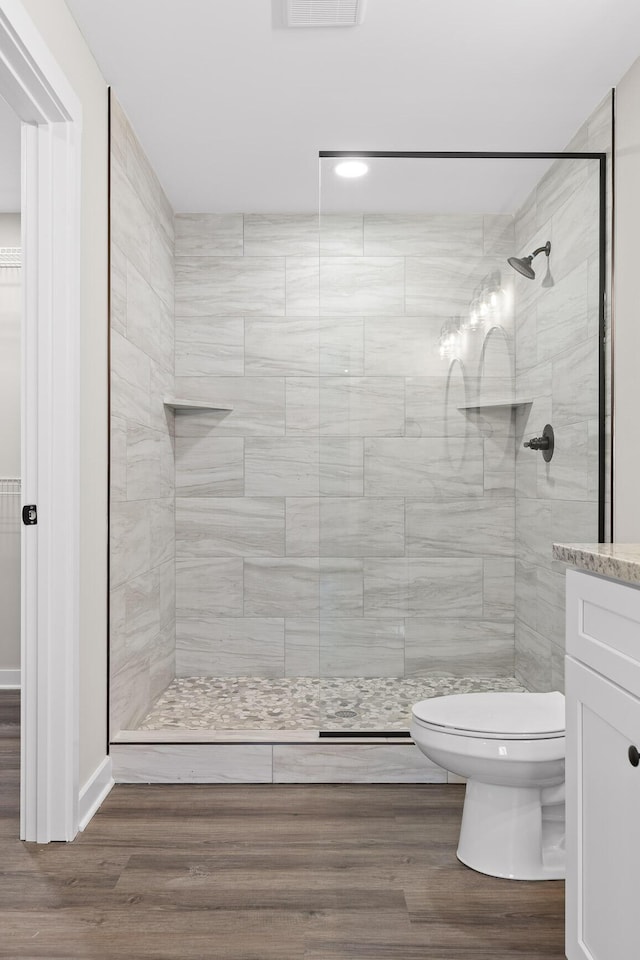 bathroom featuring tiled shower, toilet, vanity, and wood finished floors