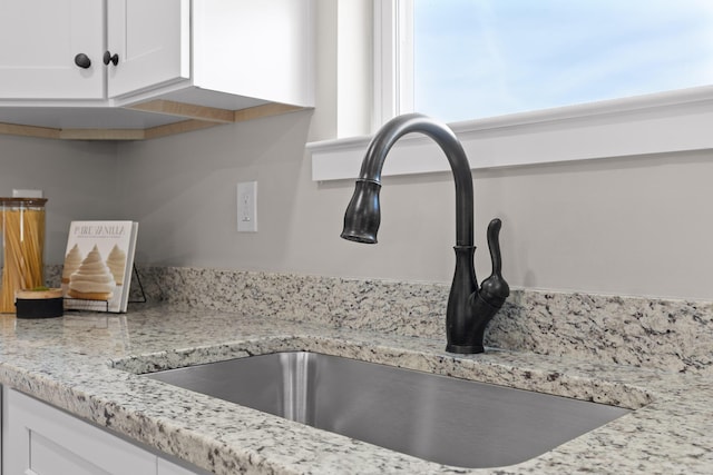 details with white cabinets, light stone counters, and a sink