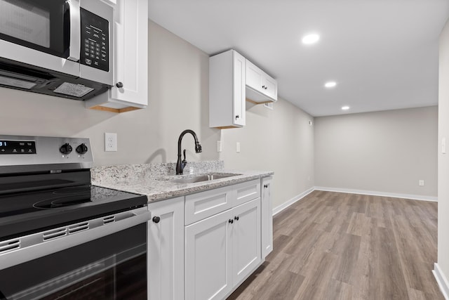 kitchen featuring light wood-type flooring, a sink, stainless steel appliances, white cabinets, and light stone countertops