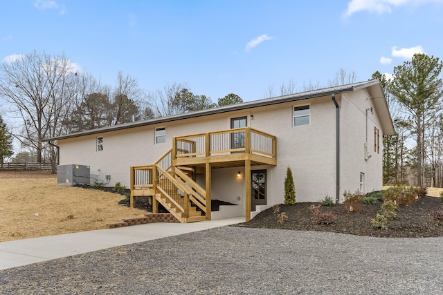 back of house with stucco siding, central air condition unit, a wooden deck, and stairs