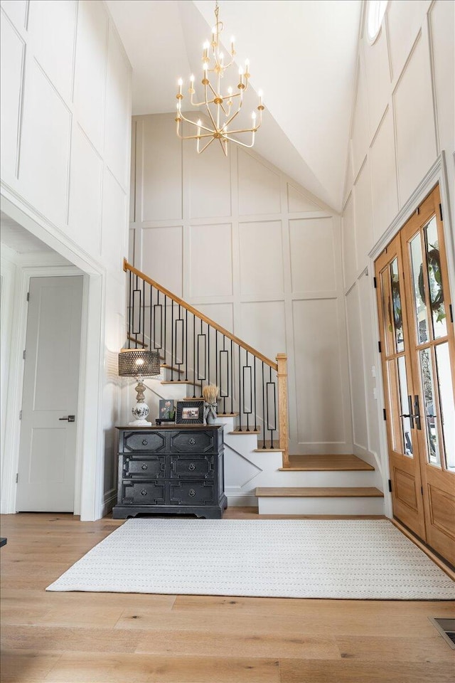 foyer featuring a chandelier, stairway, wood finished floors, a decorative wall, and high vaulted ceiling