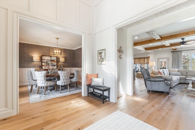 living area featuring beam ceiling, a decorative wall, baseboards, and light wood-type flooring