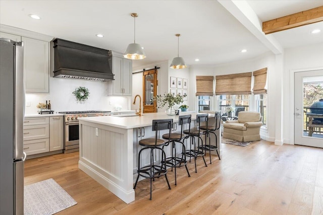 kitchen with light wood-type flooring, light countertops, custom exhaust hood, stainless steel appliances, and a sink