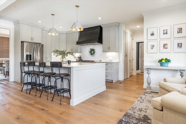 kitchen featuring custom exhaust hood, light wood finished floors, a breakfast bar, and stainless steel fridge with ice dispenser