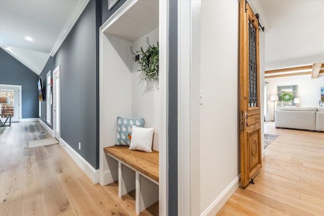 corridor featuring a barn door, baseboards, lofted ceiling, and light wood-style flooring