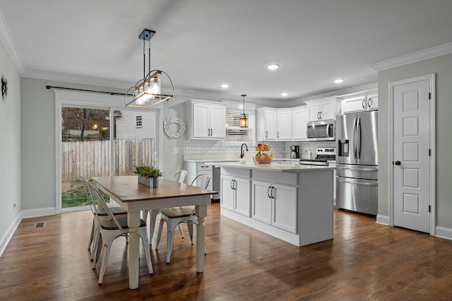 kitchen with light countertops, white cabinets, appliances with stainless steel finishes, crown molding, and a center island