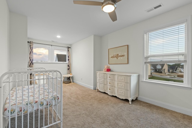 bedroom featuring a ceiling fan, baseboards, visible vents, a crib, and light carpet