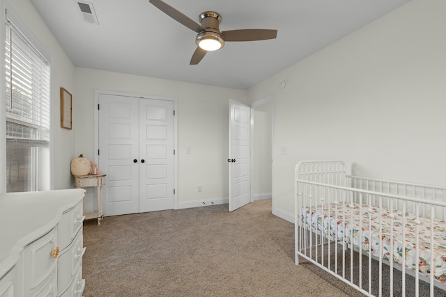 bedroom with visible vents, baseboards, a nursery area, a closet, and light colored carpet