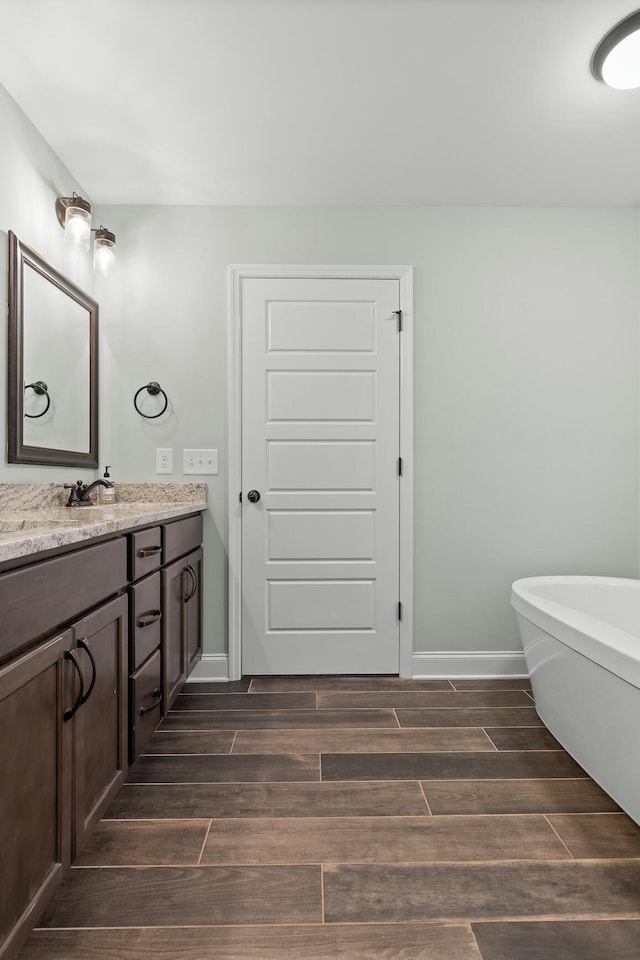 bathroom featuring vanity, a freestanding bath, baseboards, and wood tiled floor