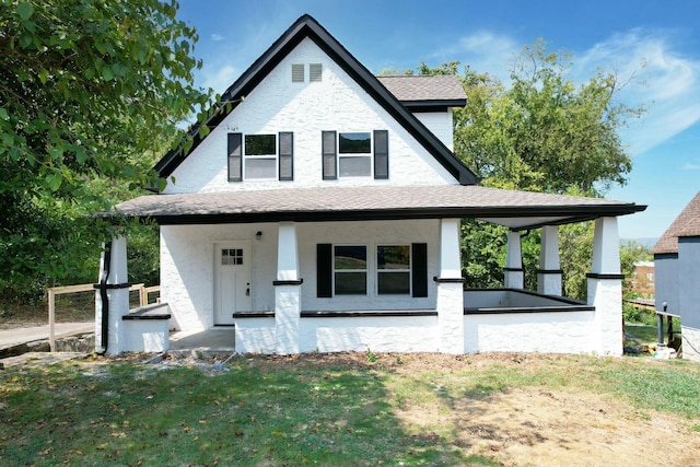 view of front facade featuring covered porch, a shingled roof, and a front lawn