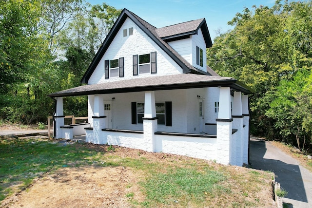 view of front of property featuring covered porch, a shingled roof, and a front lawn