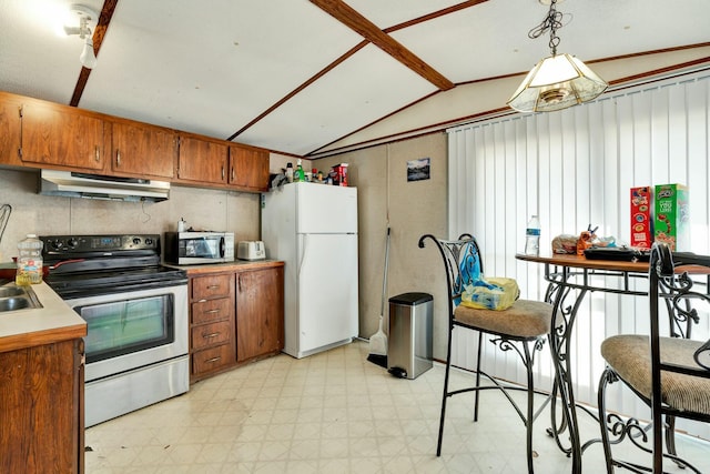 kitchen featuring light floors, vaulted ceiling, appliances with stainless steel finishes, under cabinet range hood, and brown cabinets