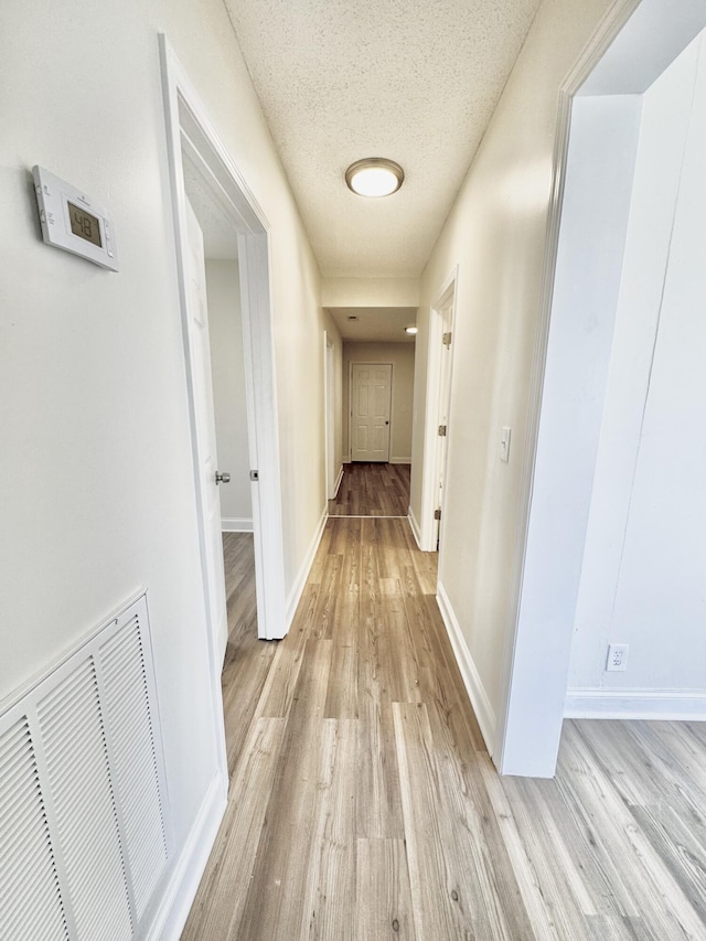 hall featuring light wood-type flooring, visible vents, baseboards, and a textured ceiling