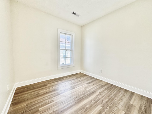 empty room with light wood-style floors, visible vents, and baseboards