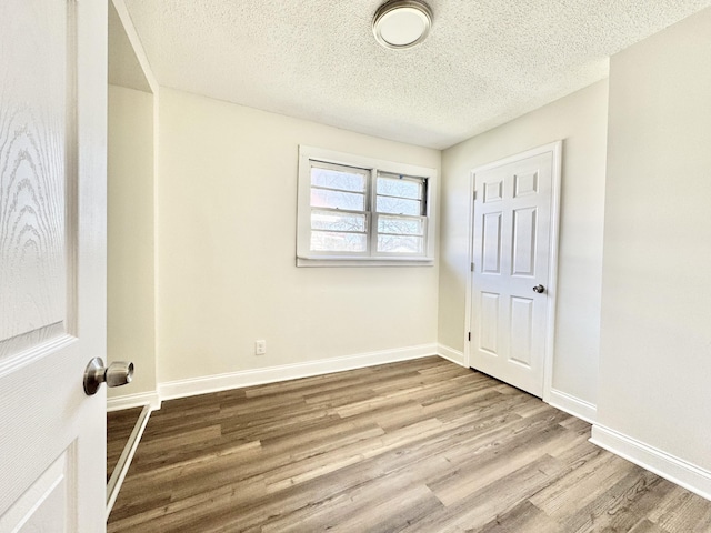 unfurnished bedroom featuring a textured ceiling, baseboards, and wood finished floors