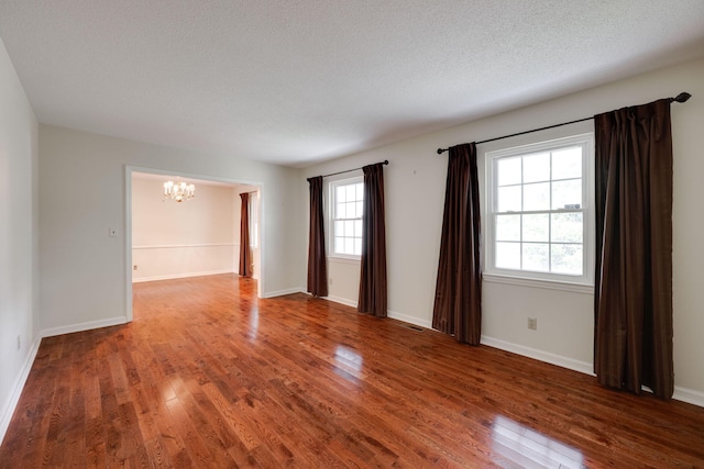 empty room featuring visible vents, a textured ceiling, an inviting chandelier, and hardwood / wood-style floors