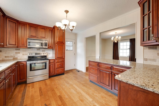 kitchen with ornamental molding, stainless steel appliances, pendant lighting, a notable chandelier, and light wood-type flooring