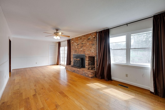 unfurnished living room with light wood finished floors, visible vents, a wood stove, and ceiling fan