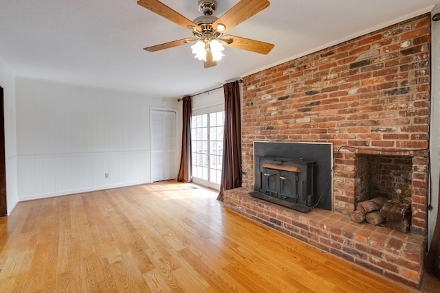 unfurnished living room with a wood stove, ceiling fan, and wood finished floors