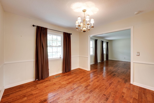 spare room featuring a wainscoted wall, a notable chandelier, light wood-style floors, and visible vents