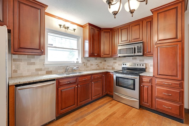 kitchen featuring a sink, stainless steel appliances, light stone counters, and light wood-style floors