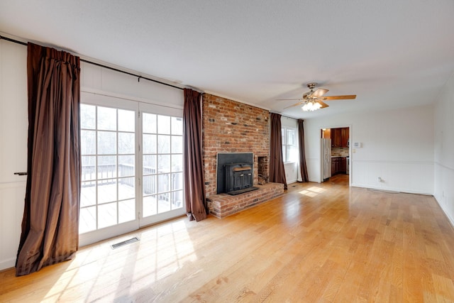 unfurnished living room with light wood finished floors, visible vents, a wood stove, and ceiling fan