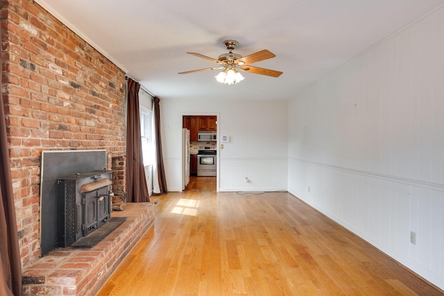 unfurnished living room with a wood stove, a ceiling fan, and light wood-type flooring