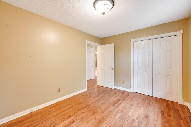 unfurnished bedroom with baseboards, light wood-type flooring, a closet, and a textured ceiling