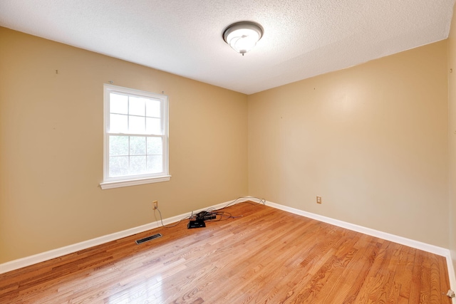 empty room with a textured ceiling, wood finished floors, visible vents, and baseboards