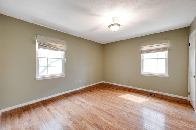 empty room with light wood-style flooring, baseboards, visible vents, and a textured ceiling